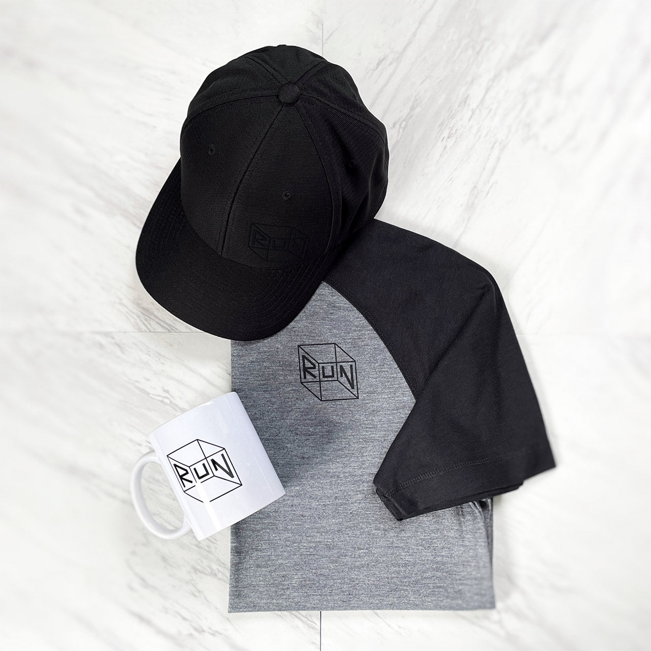 RUN gift box set from TWO CORRALS Lifestyle Running Brand with our signature RUN cube design on a heathered gray and black performance raglan tshirt, white dishwasher safe mug, and black performance hat